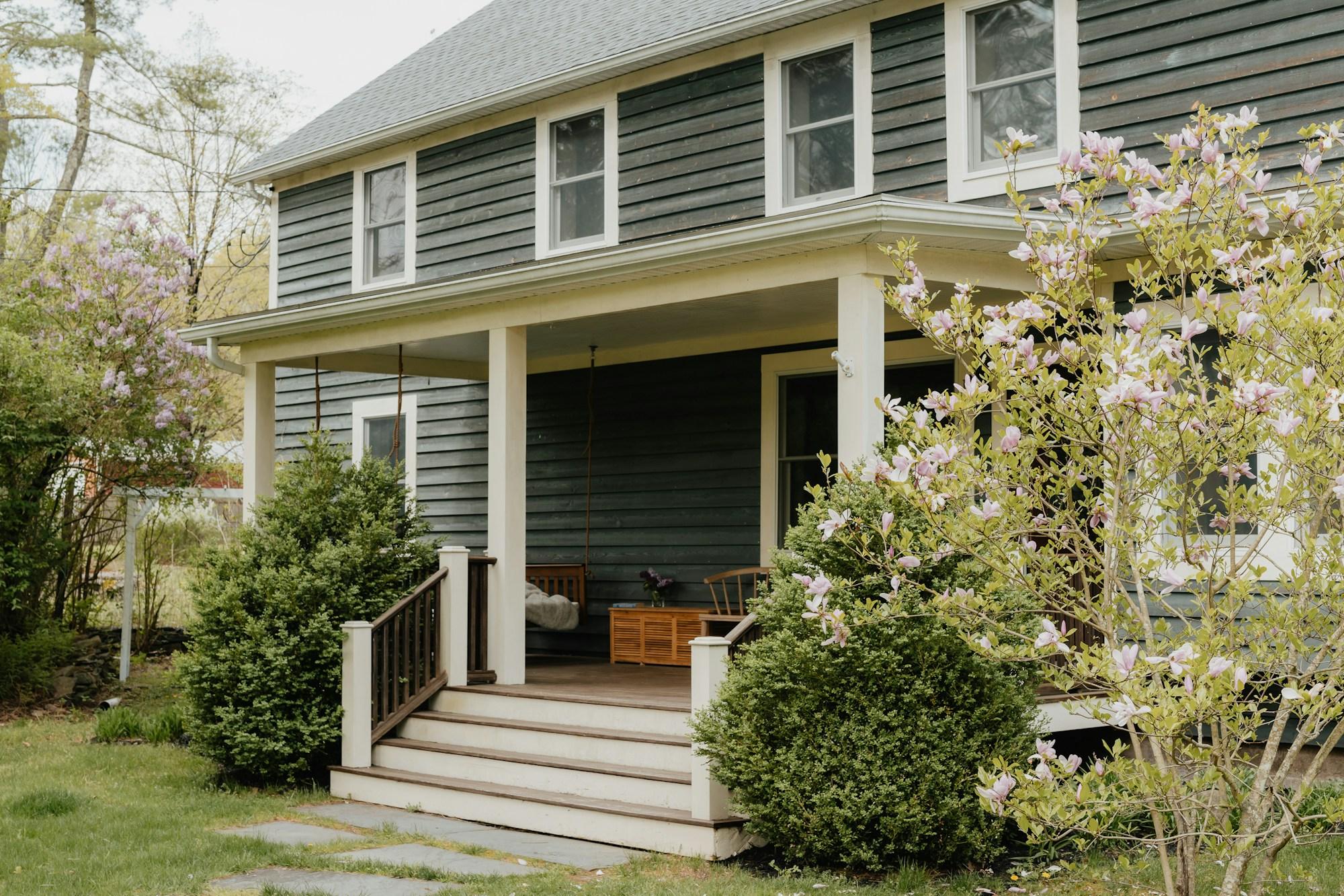 Covered porch addition on a green clapboard house, with a porch swing, painted columns and steps down to the garden.