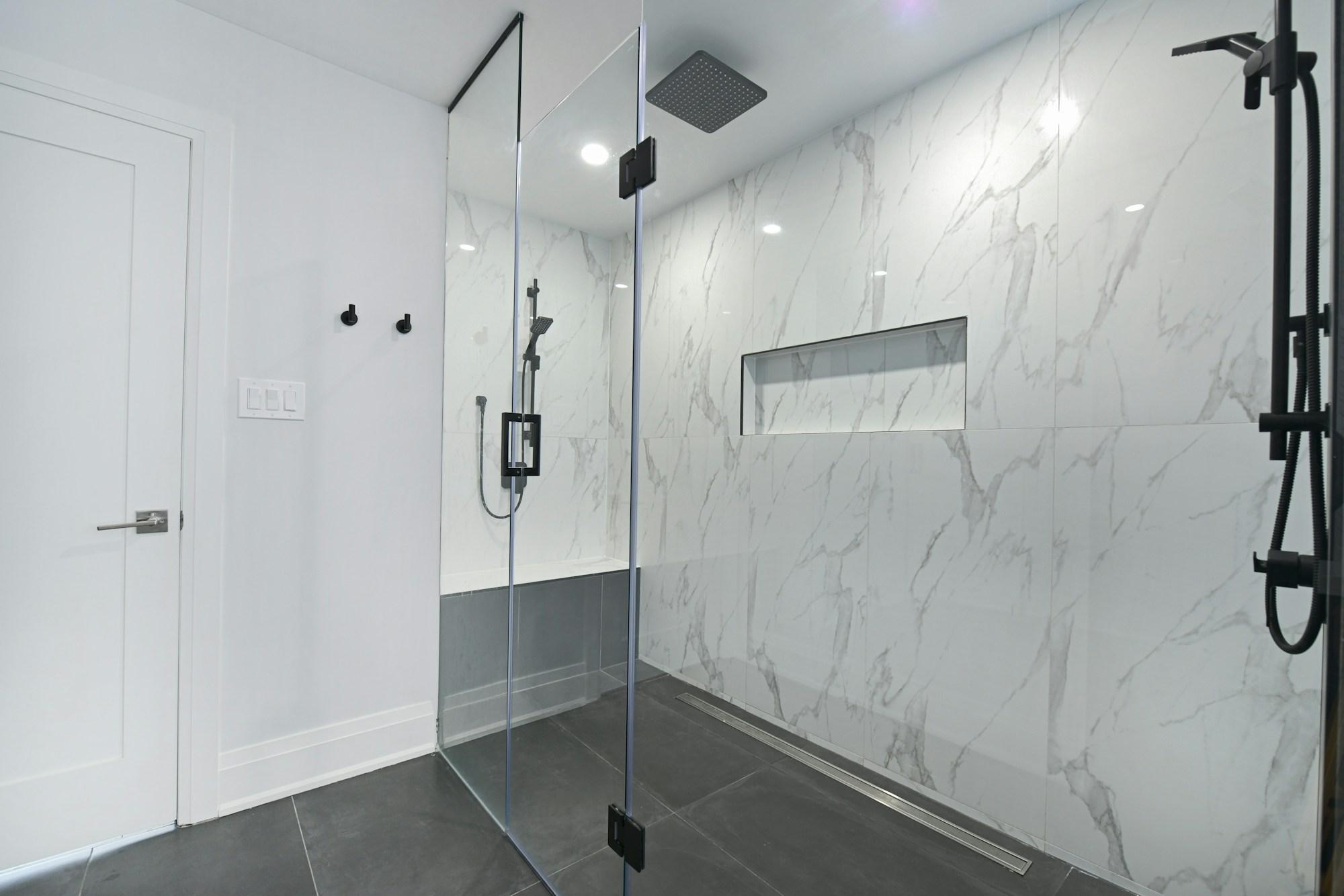 Reconfigured bathroom with a curbless walk-in shower, marble-effect large-format tile, a linear floor drain and matt black fittings.